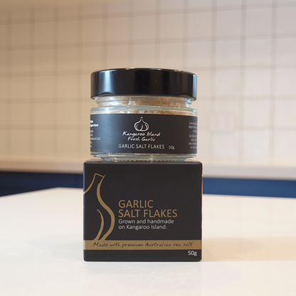 A jar of Kangaroo Island Fresh Garlic Salt and its matching black cardboard box, displayed on a white countertop with a tiled kitchen background.