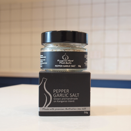 A jar of Kangaroo Island Fresh Garlic Pepper Garlic Salt with its black cardboard packaging box, displayed on a white countertop with a tiled kitchen background.